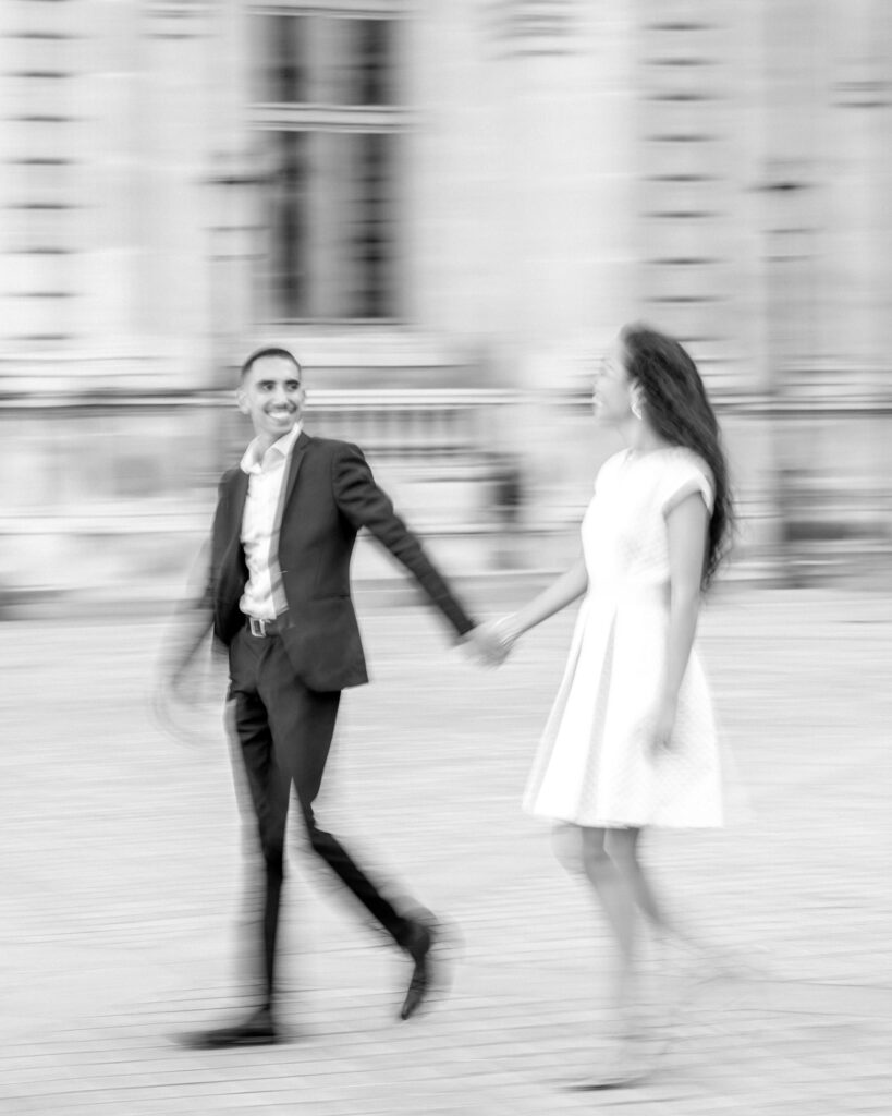 Black & white blurred motion photo of bride and groom walking by the Louvre museum in Paris