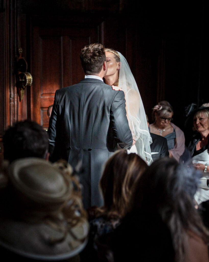 Dark & moody style wedding photo of bride and groom having their first kiss as husband and wife