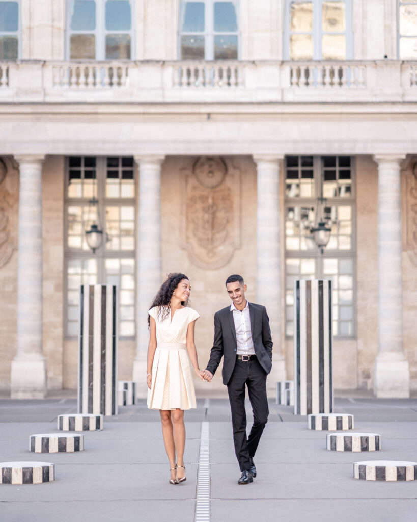Couple walking hand in hand throught the black and white columns at the courtyard of honour at the Palais Royale in Paris