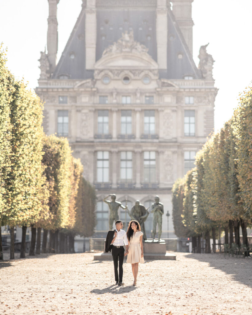 Bride and groom walking down tree lined pathway in front of the louvre in the Jardin des Tuileries
