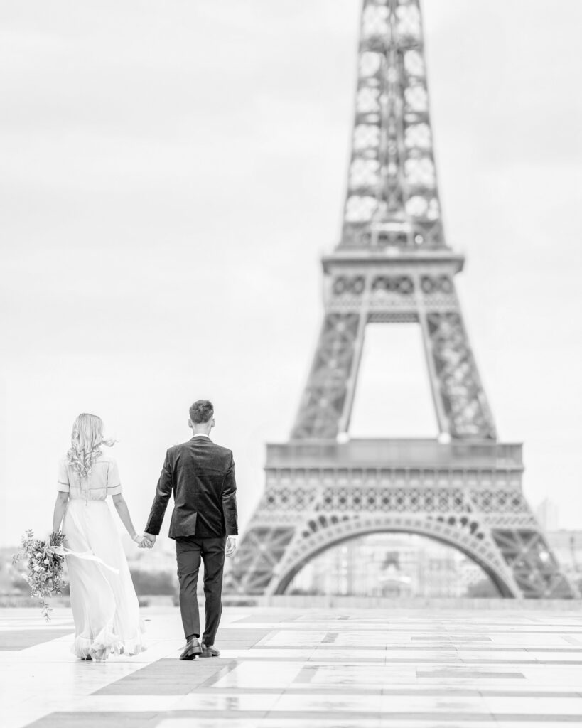 Bride and groom walking and holding hands along the trocadero in front of the Eiffel Tower