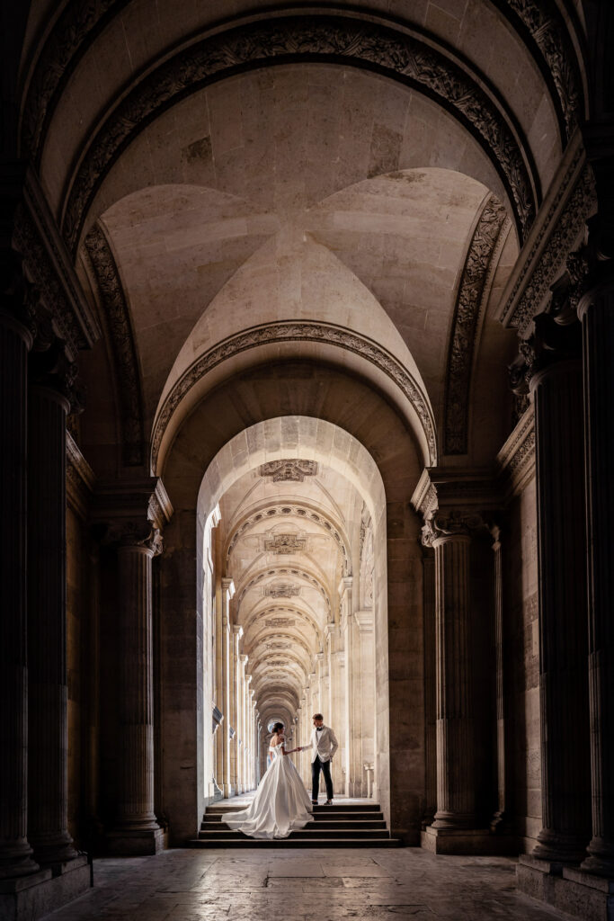 Bride and groom posing together in one of the covered archways at the Louvre museum in Paris