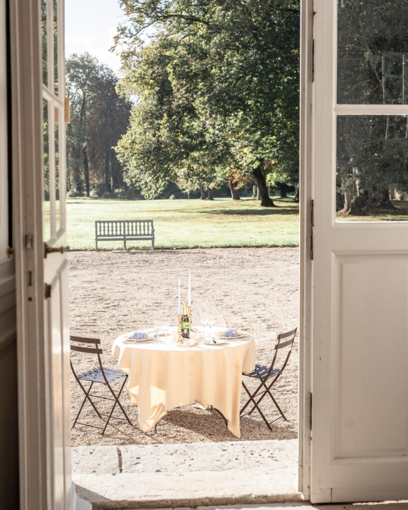 Looking through the front door out into the garden and a breakfast table for 2 on the terrace at Chateau de Courtomer in Normandy, France.