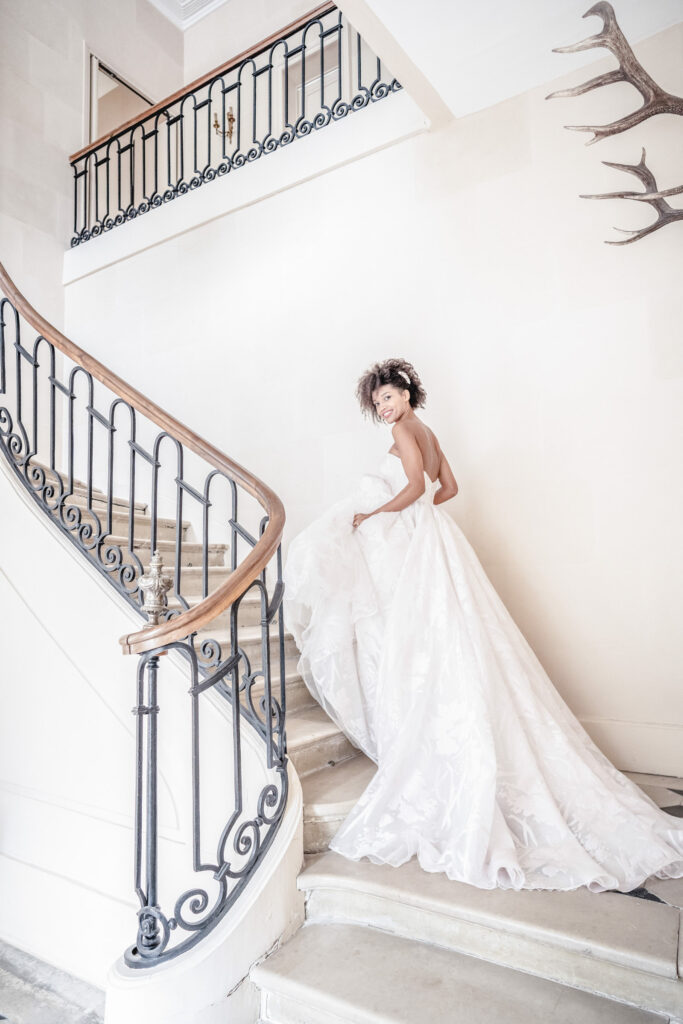 A bride wearing a ballgown style wedding dress and walking up the grand staircase at Chateau de Courtomer in Normandy, France.