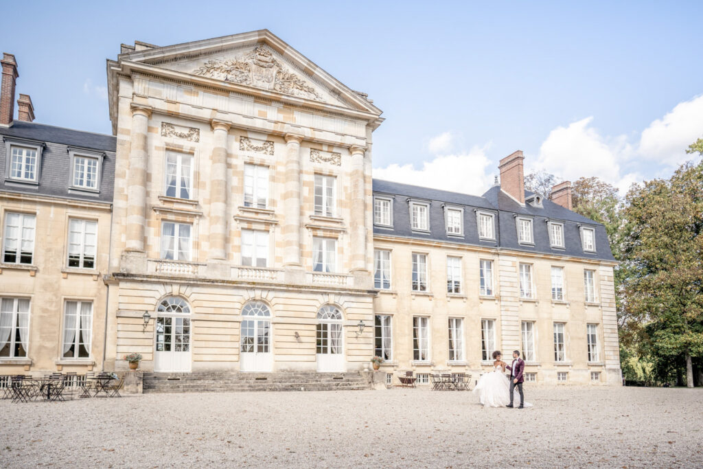 Bride and groom walking past the front exterior of wedding venue Chateau de Courtomer in Normandy, France.