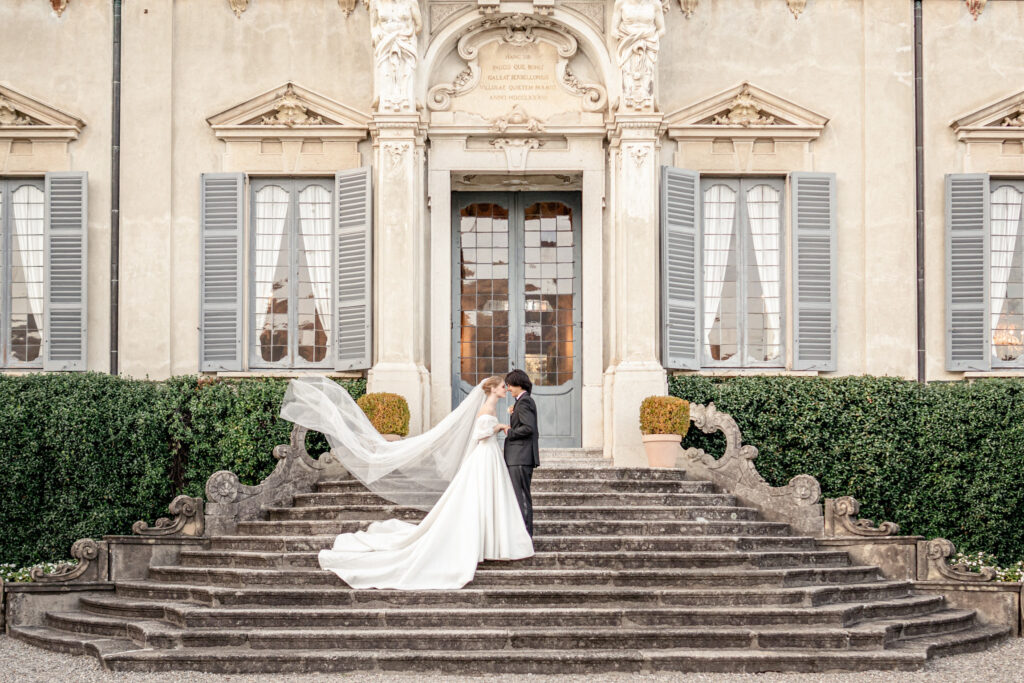 Bride and groom posing on the steps of villa sola cabiatit with the bride's veil blowing