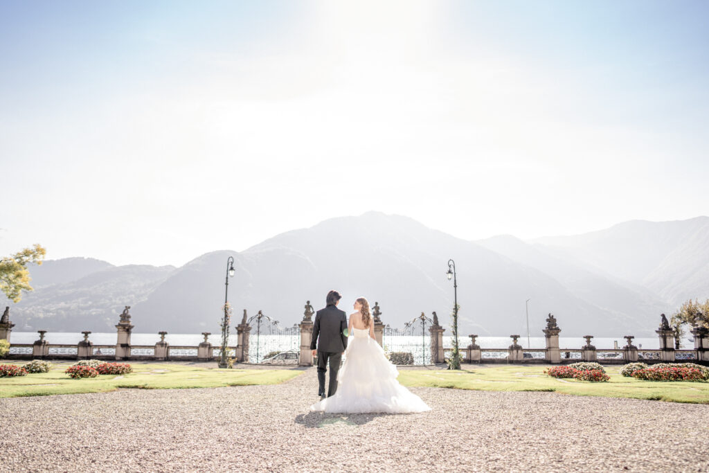 Bride and groom walking hand in hand toward Lake Como