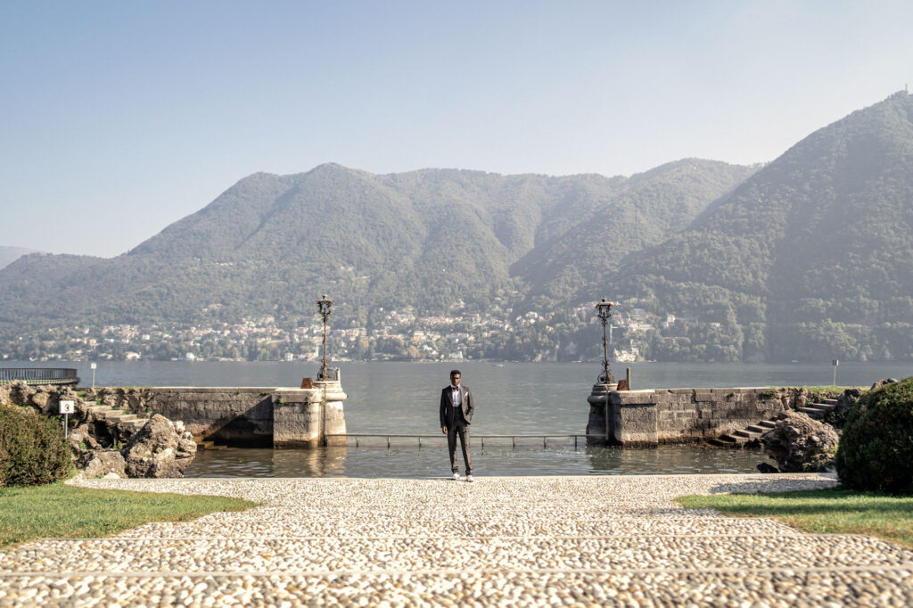 Groom posing by Lake Como within the gardens of Villa Erba wedding venue