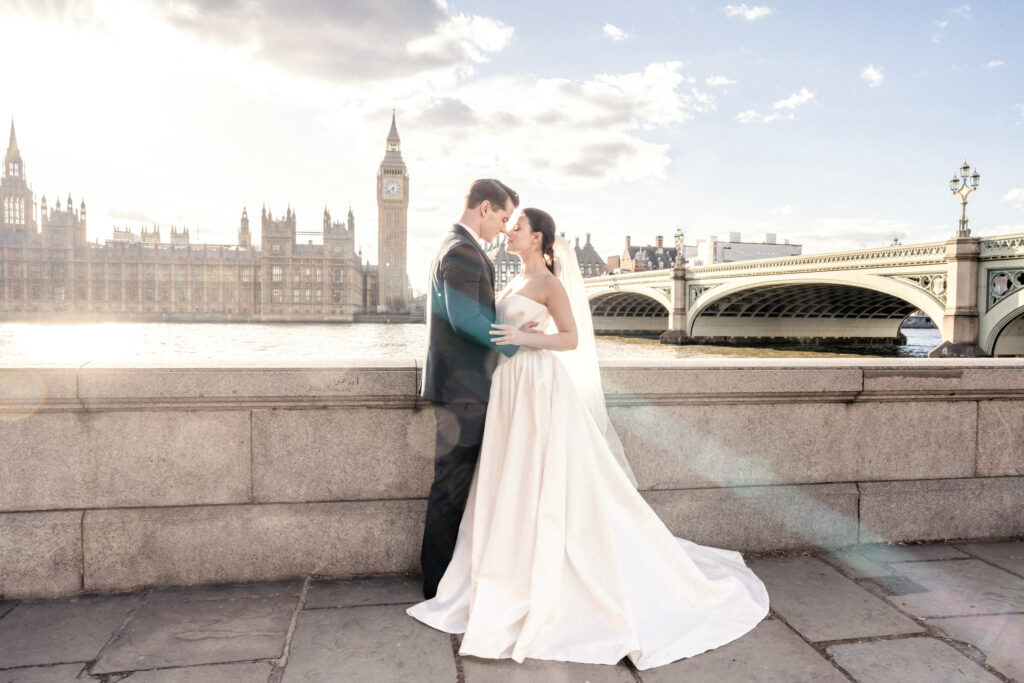 Bride and groom posing in London in front of the Houses of Parliament and Big Ben next to the River Thames in Westminster