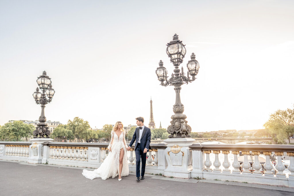 Bride and groom walking hand in hand whilst looking at each other along the Pont Alexandre III bridge in Paris in front of the Eiffel Tower