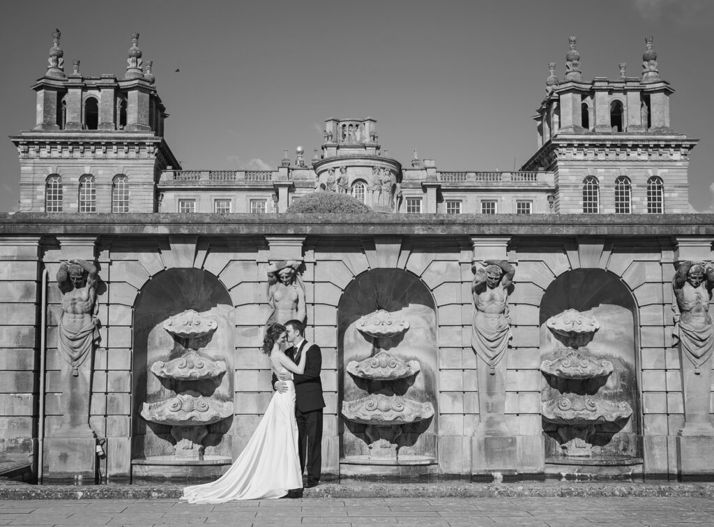 Bride and groom kissing posing in front of the water statues on the terrace at Blenheim Palace wedding venue in Oxfordshire
