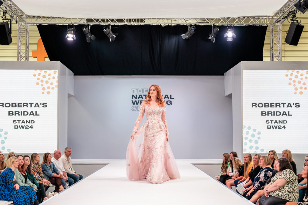 Model walking down the catwalk at the national wedding show wearing a bridal gown