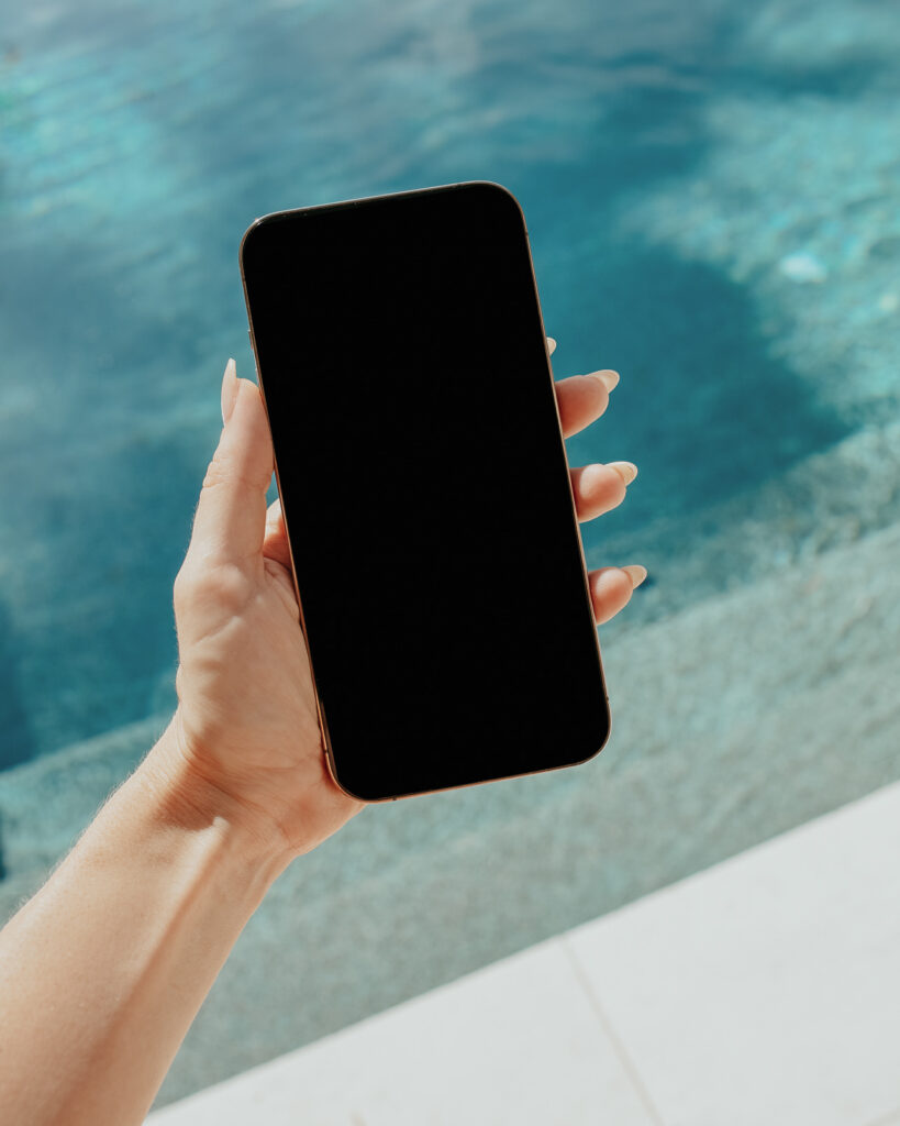 A mobile phone in hand on vacation in front of a swimming pool