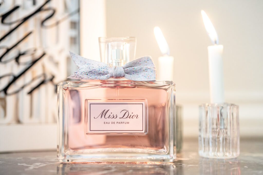 Bottle of Miss Dior perfume with candles in the background.