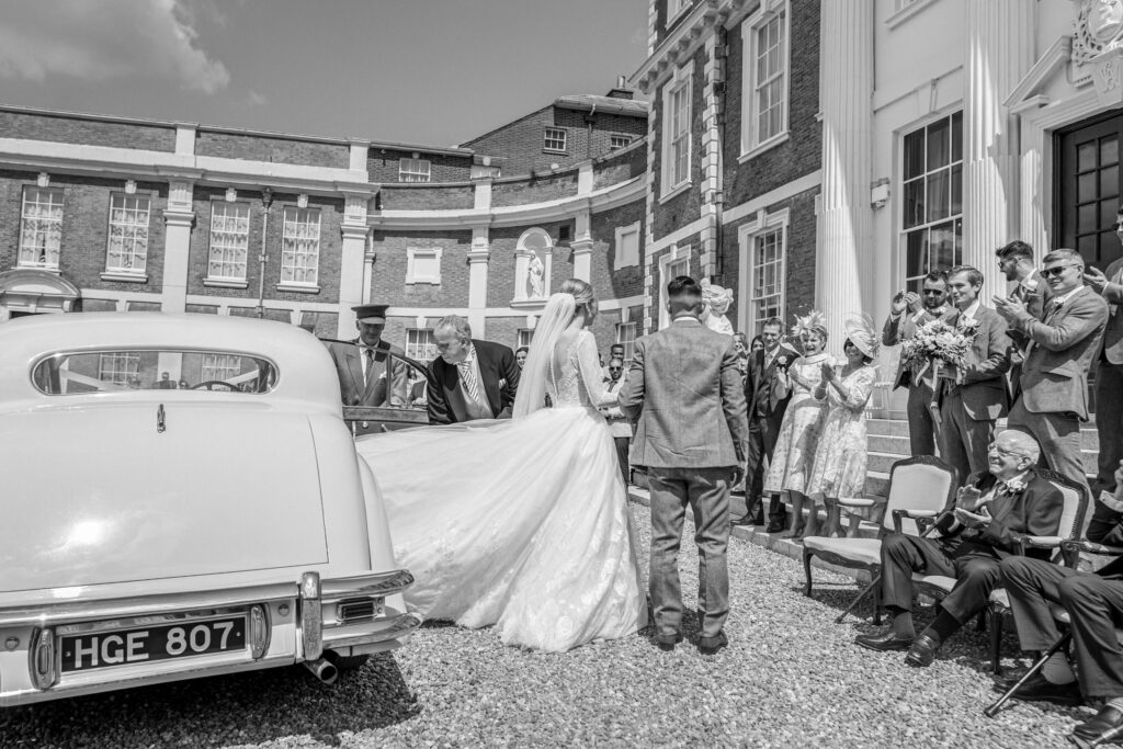 Bride and groom getting out of their wedding car to cheering crowds of wedding guests at Hawkstone Hall in Shropshire.