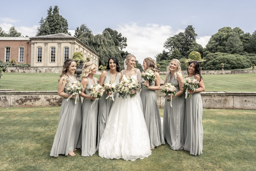 Group photo of the bride and her six bridesmaids, wearing green dresses in the gardens at Hawkstone Hall wedding venue in Shropshire.