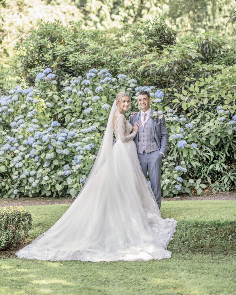 Bride and groom posing in front of blue hydrangeas in the gardens at Hawkstone Hall wedding venue in Shropshire.