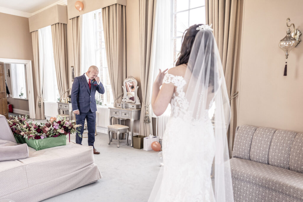 Father of the bride crying as he sees his daughter for the first time as a bride in the Bronte Suite bridal room at Hawkstone Hall wedding venue in Shropshire.