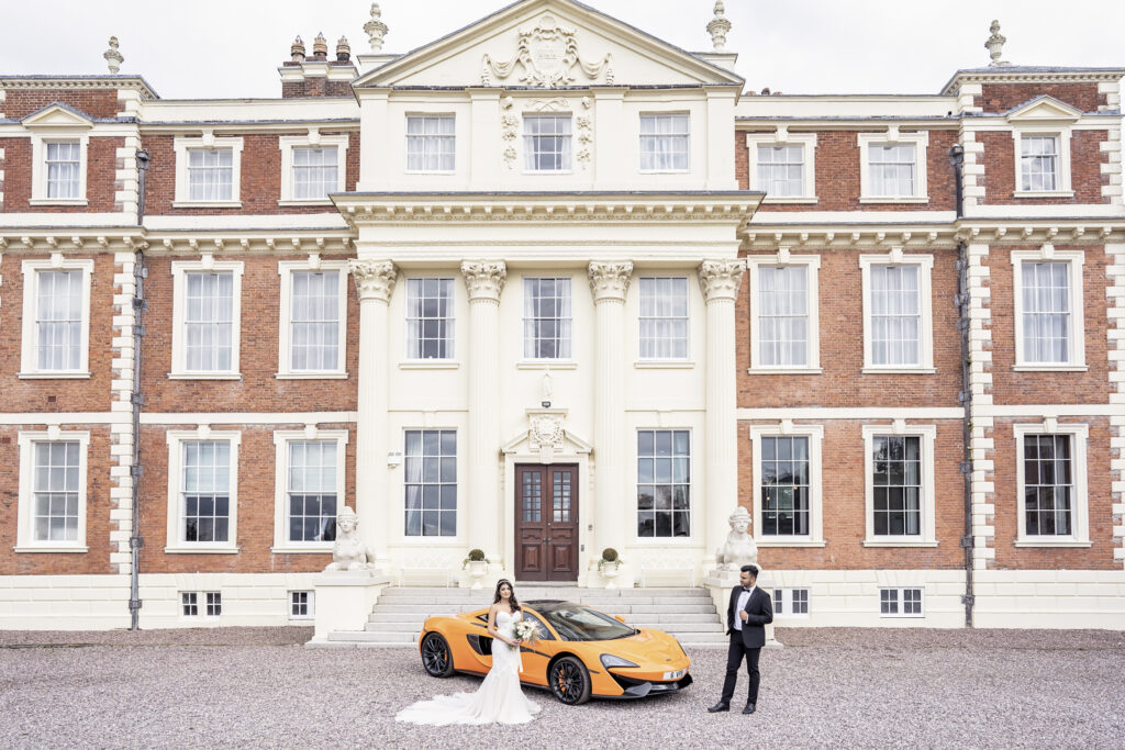 Exterior of Hawkstone Hall Shropshire wedding venue to the front with maclaren sports car and bride and groom