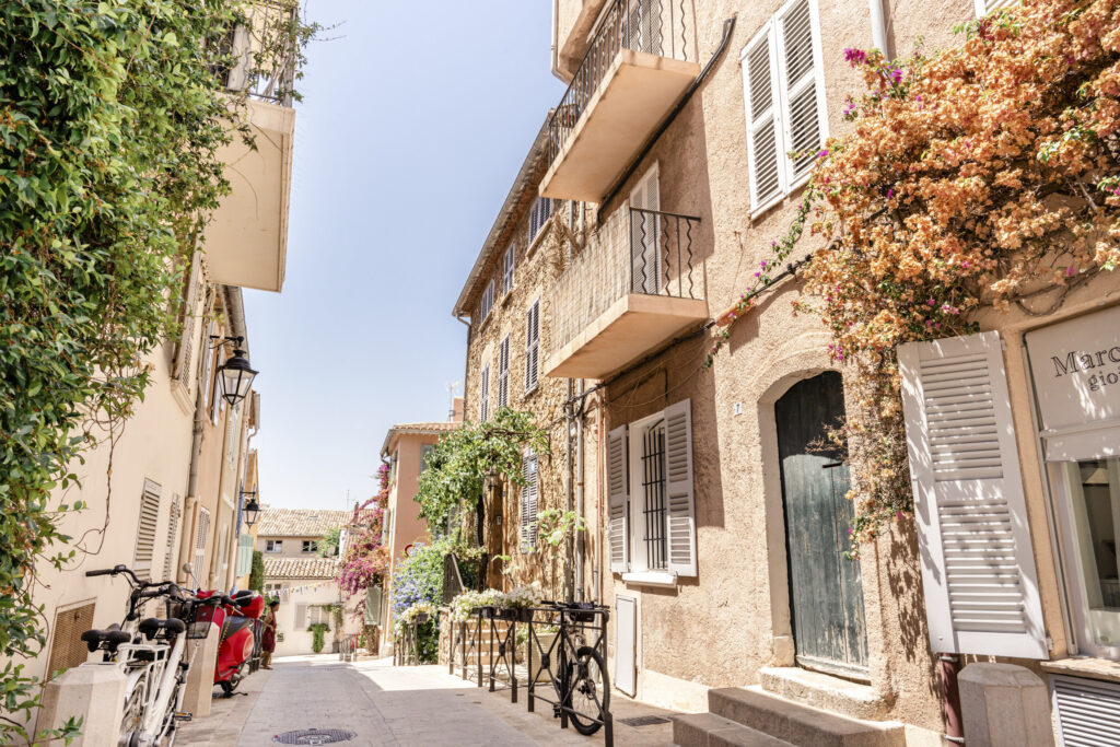 A quaint French street in Saint Tropez with climbing flowers and shutters.
