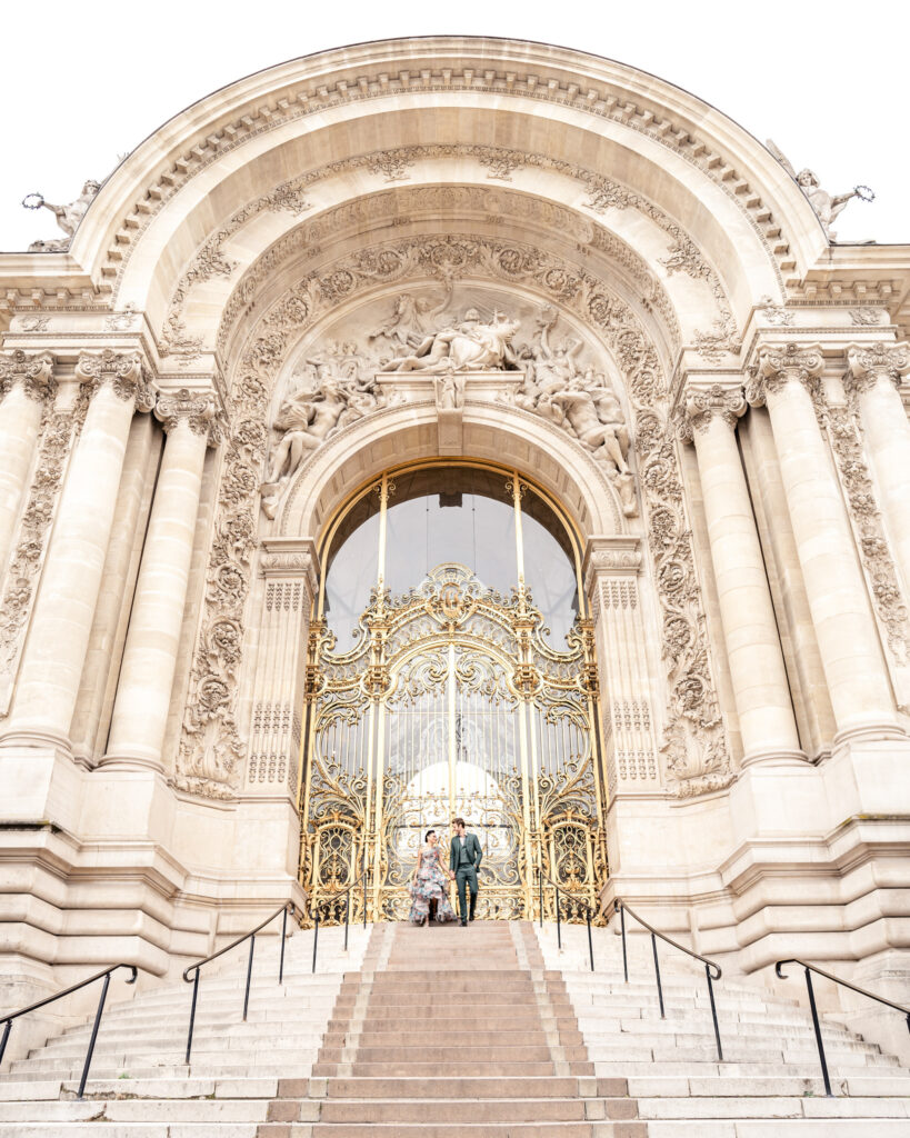 A bride and groom walking down the steps of the petit palais in front of the gold gate in Paris