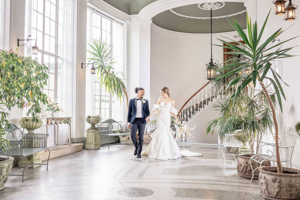 Bride and groom walking hand in hand through the Winter Garden room at Hawkstone Hall in Shropshire.