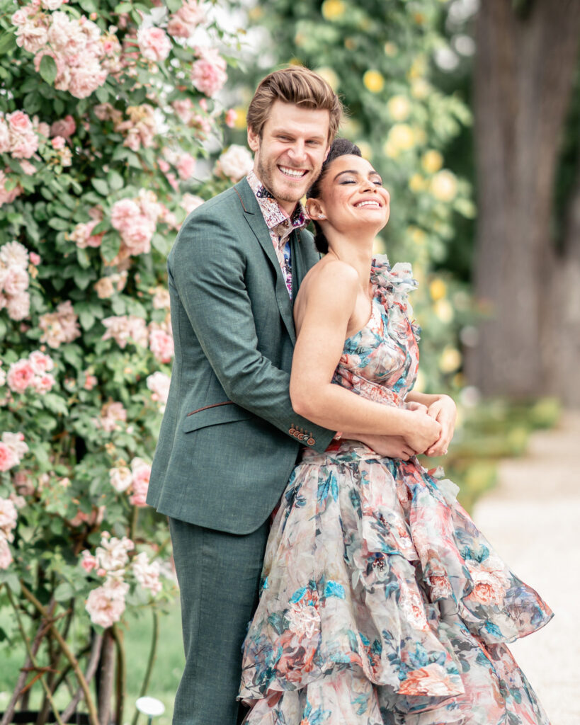 A bride and groom to be hugging next to a rose bush in a Paris park.