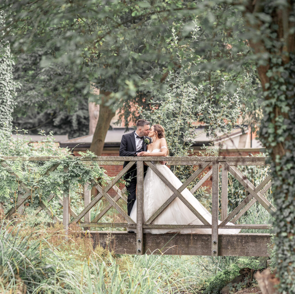 Bride and groom kissing on the bridge in the gardens of Tyn Dwr Hall in Wales.