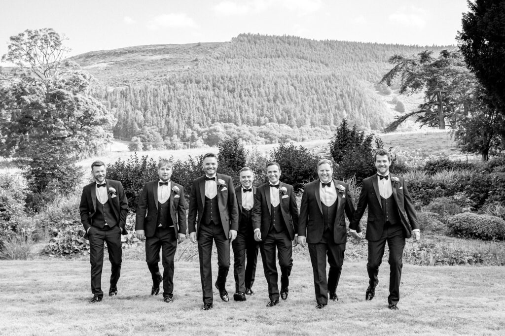 Groom and her groomsmen posing together for a group photograph in the gardens of Tyn Dwr Hall.