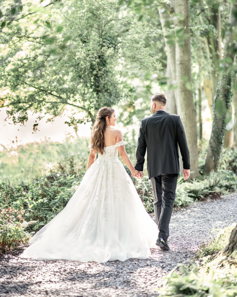 Bride and groom walking hand in hand through the forest walkthrough at Tyn Dwr Hall in Wales.