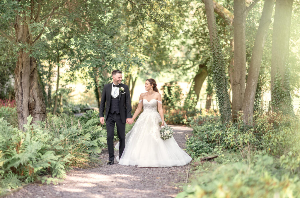 Bride and groom walking hand in hand through the woodland path at Tyn Dwr Hall