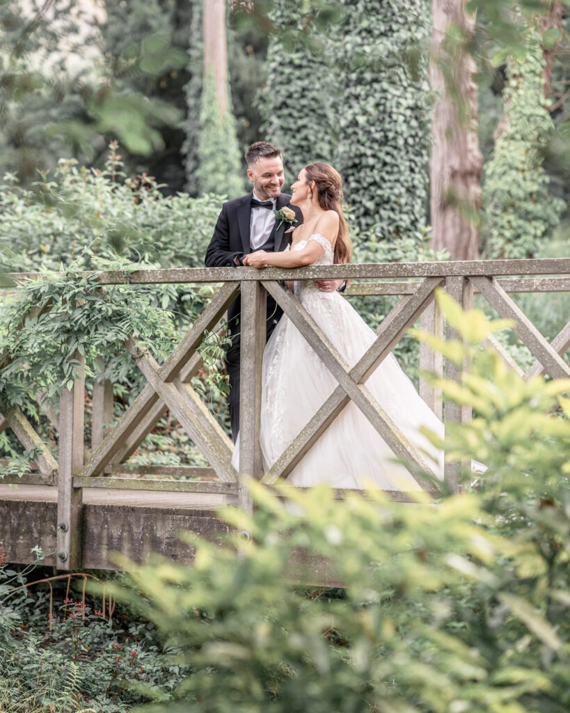 Bride and groom standing on one of the outdoor wooden bridge over the babbling stream in the grounds of Tyn Dwr Hall.