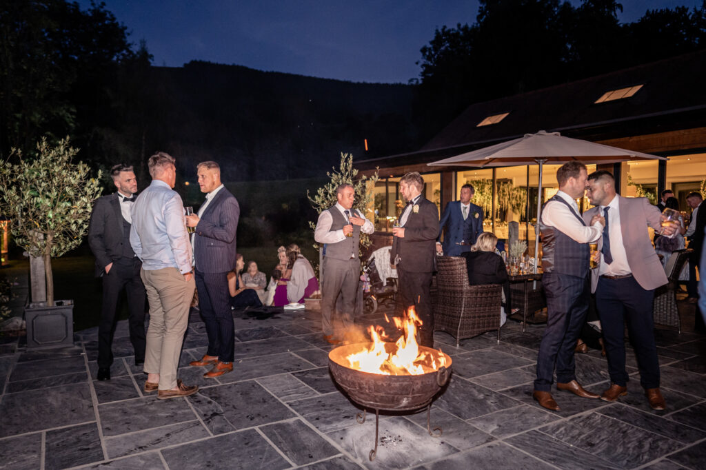 Wedding guests on the outdoor terrace at Tyn Dwr Hall in the evening by the firepit