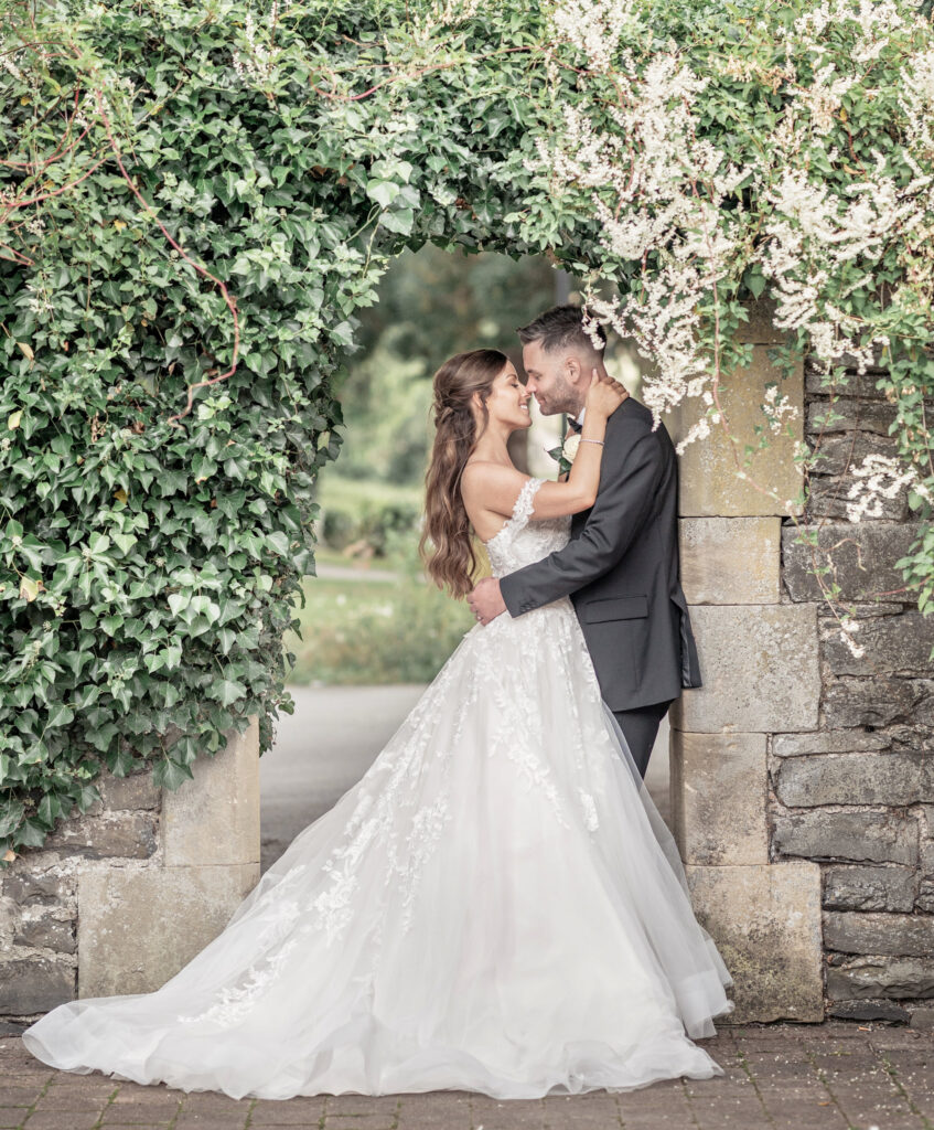 Bride and groom posing together under the stone wall arch at Tyn dwr Hall.