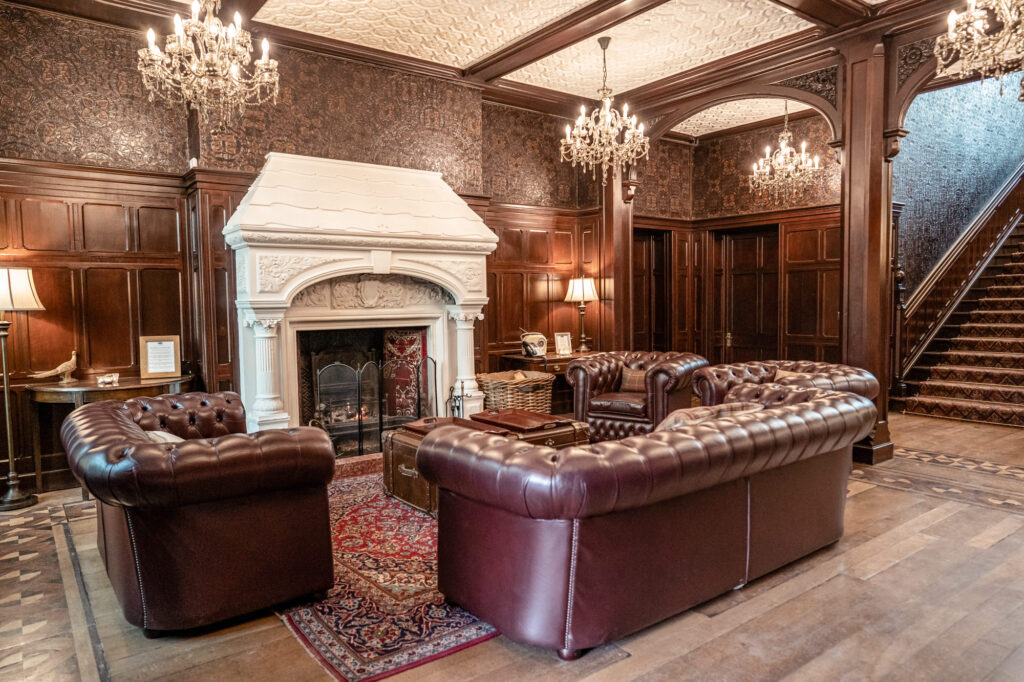 The front reception room at Tyn Dwr Hall with leather chesterfield sofas, chandeliers, fireplace, and staircase.