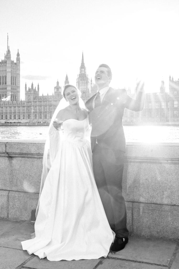 Bride and groom raising a glass of champagne to the camera in front of Big Ben and the Houses of Parliament in London
